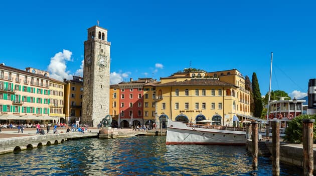 Den brede, brostensbelagte Piazza III Novembre i Riva del Garda omgivet af historiske buegange og caféer ved havnefronten